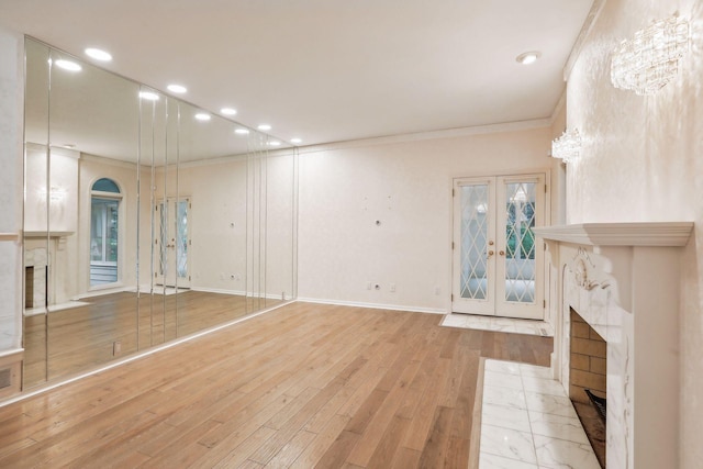 unfurnished living room featuring crown molding, light wood-type flooring, a fireplace, and french doors