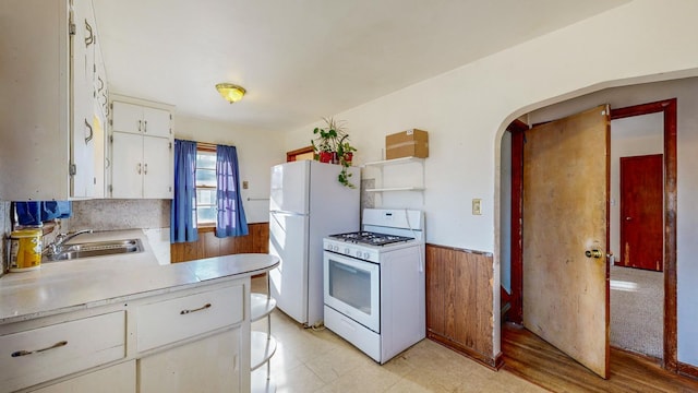 kitchen featuring white cabinetry, white appliances, sink, and wood walls