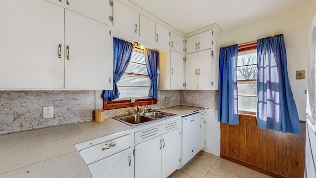 kitchen with sink, backsplash, white cabinets, light tile patterned floors, and white dishwasher