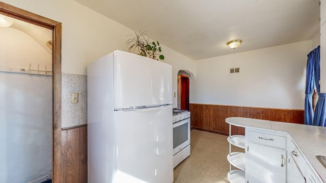 kitchen with white appliances, wood walls, and white cabinets