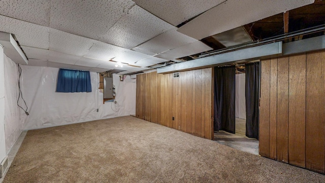 basement featuring wooden walls, electric panel, and carpet flooring