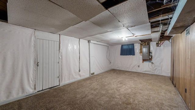 basement featuring carpet floors, electric panel, and wood walls