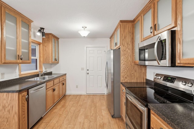 kitchen with appliances with stainless steel finishes, light hardwood / wood-style floors, sink, and a textured ceiling