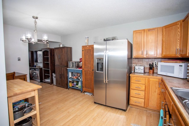 kitchen with light hardwood / wood-style flooring, decorative light fixtures, stainless steel fridge, and a chandelier