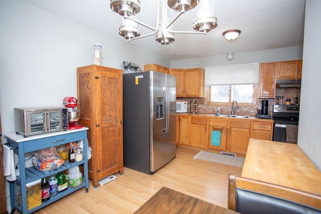 kitchen with sink, a textured ceiling, light wood-type flooring, appliances with stainless steel finishes, and a notable chandelier