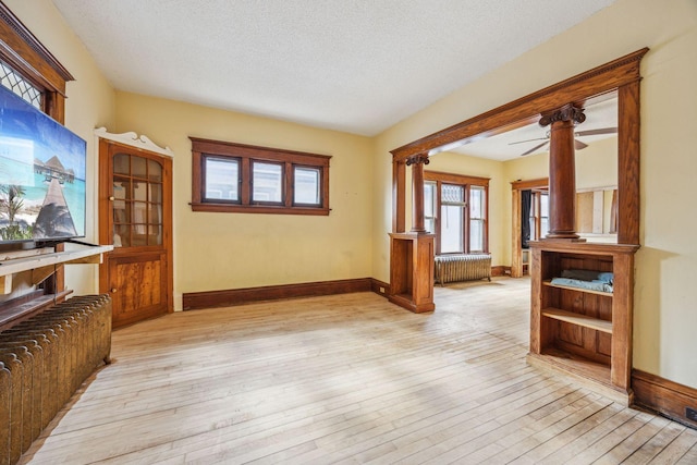 interior space with a textured ceiling, baseboards, light wood-type flooring, radiator, and ornate columns