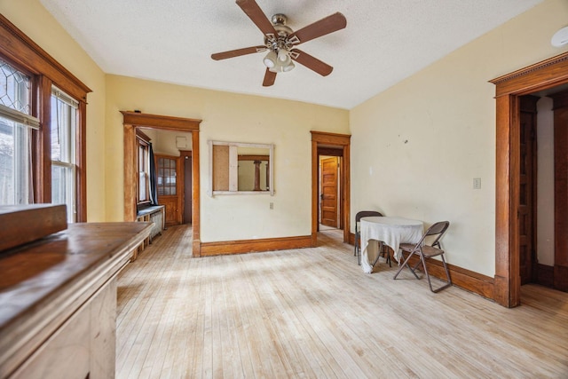 spare room featuring a textured ceiling, light wood-type flooring, a ceiling fan, and baseboards