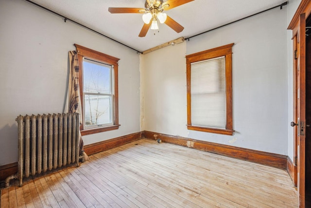 unfurnished room with baseboards, hardwood / wood-style floors, a ceiling fan, and radiator