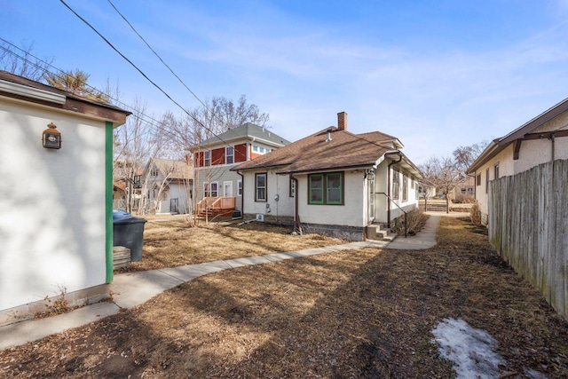 back of house with entry steps, fence, a chimney, and stucco siding