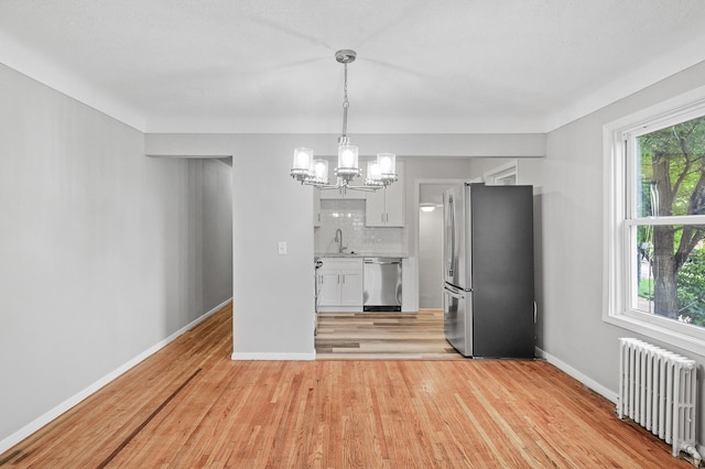 kitchen with backsplash, radiator heating unit, white cabinets, and appliances with stainless steel finishes