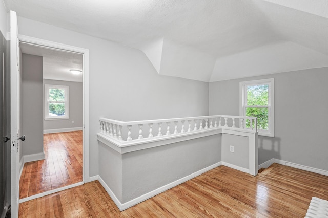 hall featuring hardwood / wood-style flooring, vaulted ceiling, and a textured ceiling