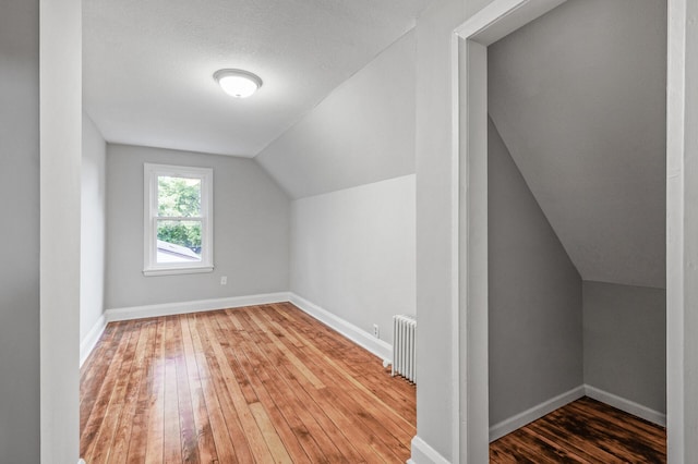 bonus room featuring radiator heating unit, dark hardwood / wood-style floors, vaulted ceiling, and a textured ceiling