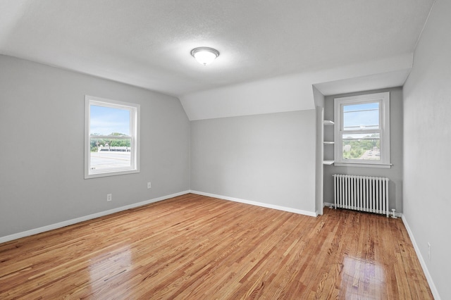 bonus room featuring light hardwood / wood-style flooring, radiator heating unit, a textured ceiling, built in shelves, and vaulted ceiling