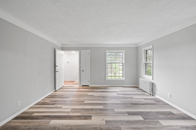 spare room featuring radiator, a textured ceiling, and light wood-type flooring