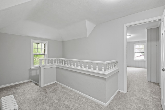 unfurnished bedroom with multiple windows, radiator heating unit, light carpet, and vaulted ceiling