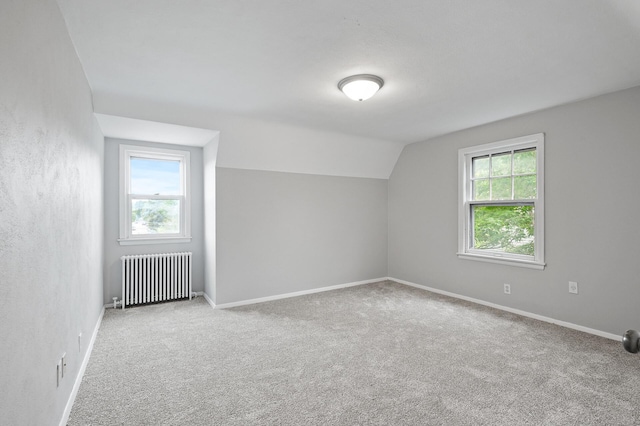 additional living space with lofted ceiling, a wealth of natural light, radiator heating unit, and light colored carpet