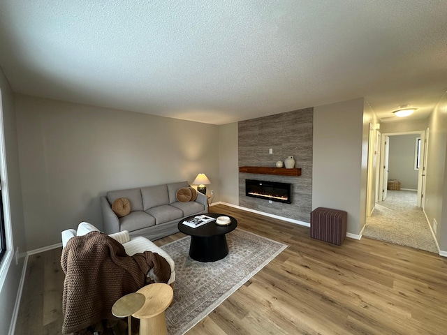 living room with a large fireplace, a textured ceiling, and light hardwood / wood-style flooring