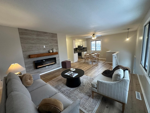 living room with light hardwood / wood-style flooring, a large fireplace, and a textured ceiling