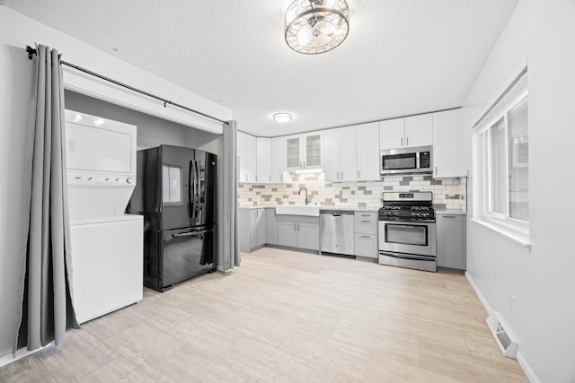 kitchen featuring backsplash, stainless steel appliances, sink, and stacked washer and clothes dryer