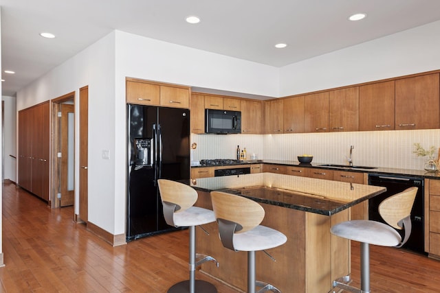 kitchen with dark wood-type flooring, black appliances, a breakfast bar, a sink, and decorative backsplash