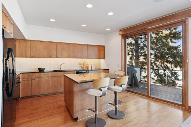 kitchen with black appliances, light wood-style flooring, a sink, tasteful backsplash, and a breakfast bar area