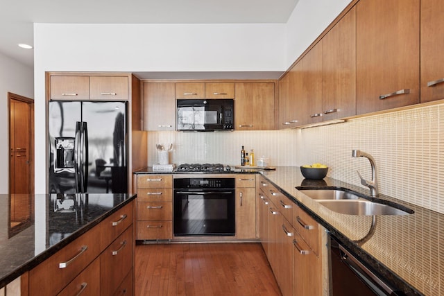 kitchen featuring dark stone counters, dark wood-style flooring, a sink, black appliances, and tasteful backsplash