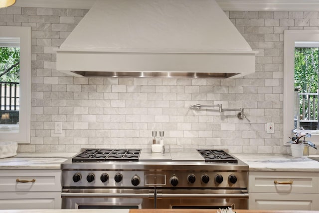 kitchen featuring custom exhaust hood, white cabinetry, backsplash, and high end range