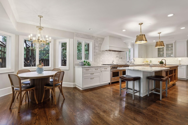 kitchen featuring a kitchen island, white cabinetry, high end range, hanging light fixtures, and custom range hood