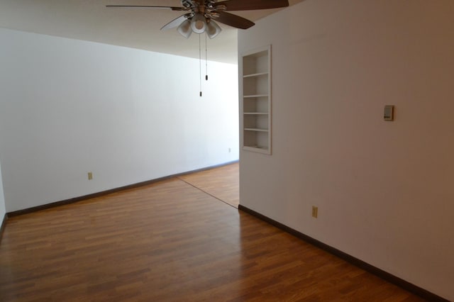 unfurnished room featuring built in shelves, wood-type flooring, and ceiling fan