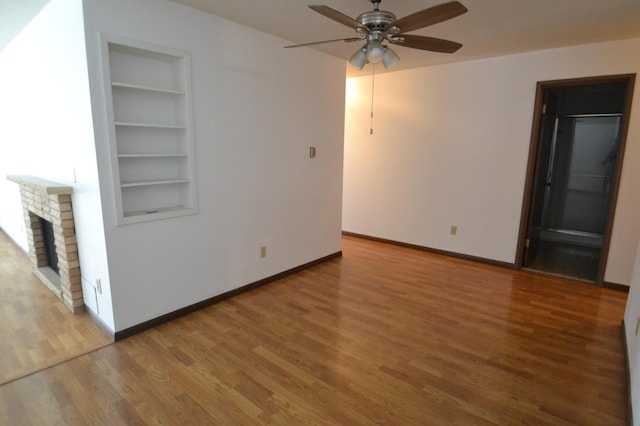 unfurnished living room with built in shelves, ceiling fan, a fireplace, and hardwood / wood-style flooring