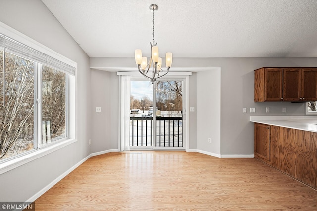 unfurnished dining area with vaulted ceiling, an inviting chandelier, a textured ceiling, and light hardwood / wood-style floors