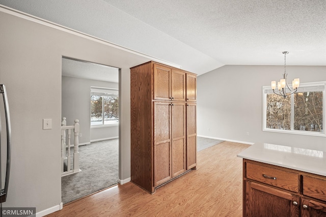 kitchen featuring decorative light fixtures, lofted ceiling, light wood-type flooring, a chandelier, and a textured ceiling