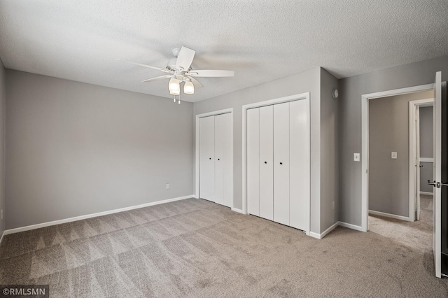 unfurnished bedroom with two closets, light colored carpet, a textured ceiling, and ceiling fan