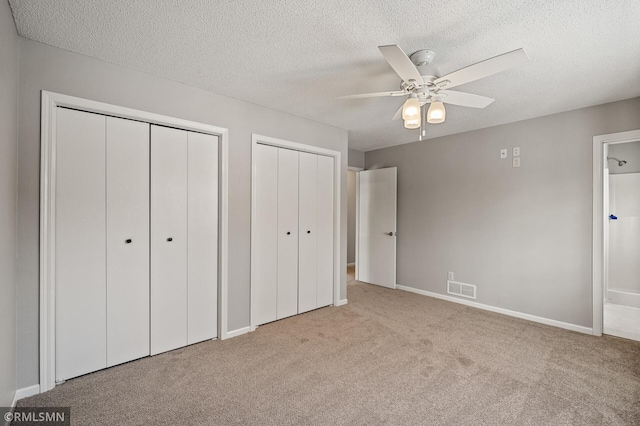 unfurnished bedroom with ceiling fan, light colored carpet, a textured ceiling, and two closets