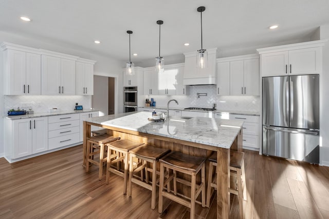 kitchen featuring white cabinetry, stainless steel appliances, a kitchen breakfast bar, a center island with sink, and decorative light fixtures