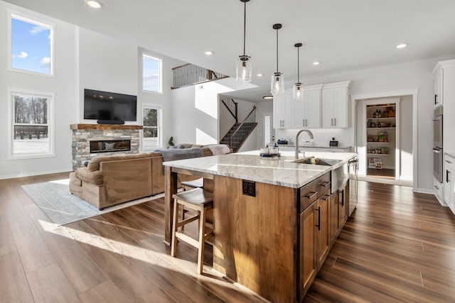 kitchen featuring pendant lighting, white cabinetry, light stone countertops, a center island with sink, and a stone fireplace