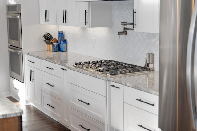 kitchen featuring appliances with stainless steel finishes, dark hardwood / wood-style floors, white cabinets, backsplash, and light stone countertops