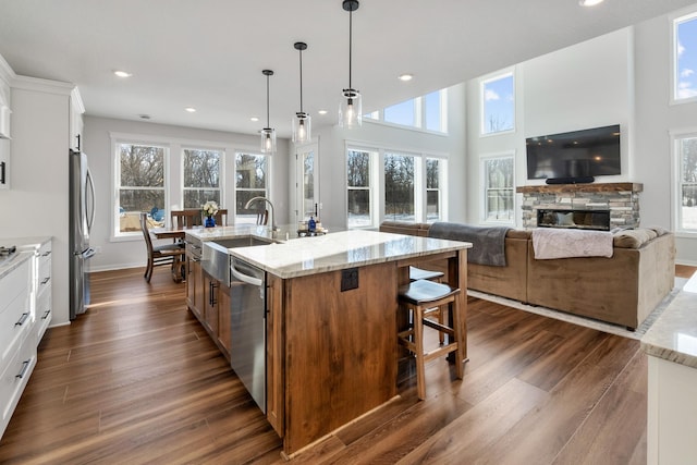 kitchen with light stone counters, hanging light fixtures, appliances with stainless steel finishes, an island with sink, and white cabinets