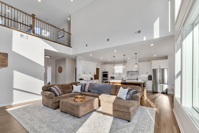 living room with sink, a towering ceiling, and light wood-type flooring