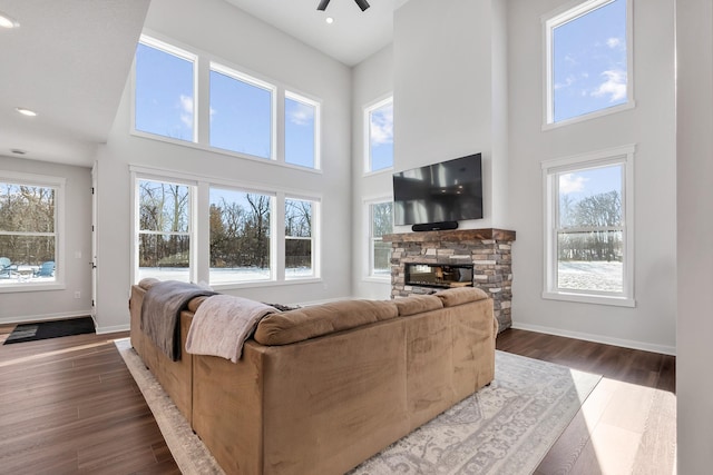 living room featuring plenty of natural light, a towering ceiling, dark wood-type flooring, and a fireplace