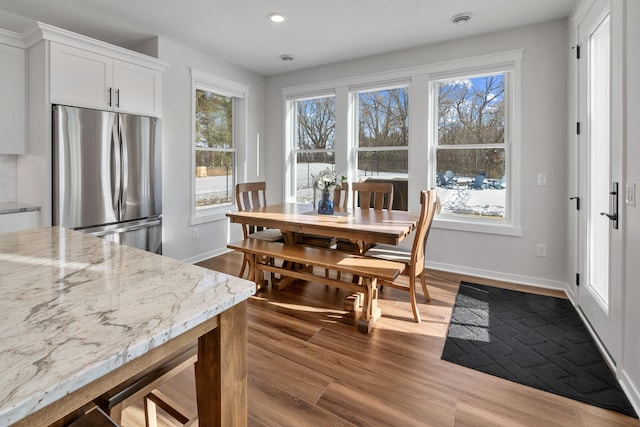 kitchen with white cabinetry, light wood-type flooring, stainless steel refrigerator, plenty of natural light, and light stone countertops