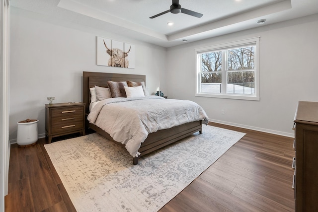 bedroom featuring dark hardwood / wood-style floors, ceiling fan, and a tray ceiling