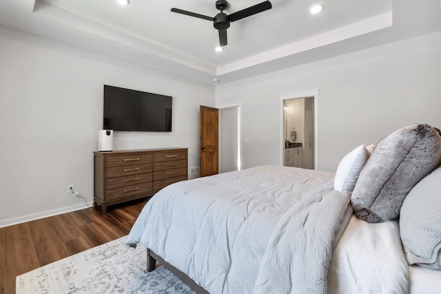 bedroom featuring ensuite bath, dark wood-type flooring, a raised ceiling, and ceiling fan