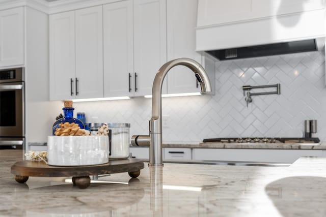 details featuring light stone counters, sink, tasteful backsplash, and white cabinets