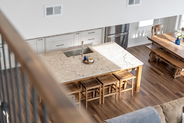 kitchen featuring sink, white cabinets, dark hardwood / wood-style flooring, stainless steel fridge, and light stone counters