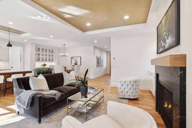 living room featuring light hardwood / wood-style flooring, a notable chandelier, a fireplace, and a tray ceiling