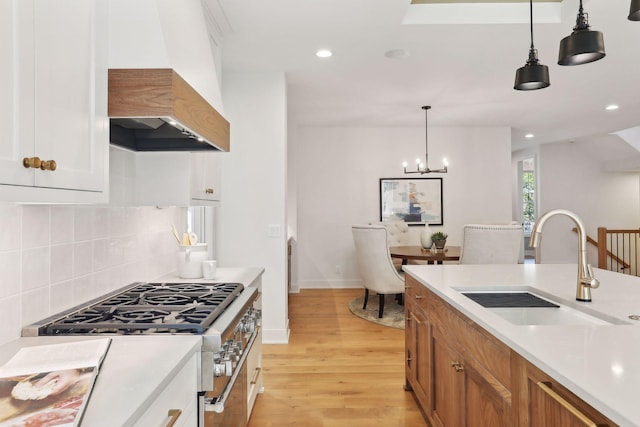 kitchen featuring pendant lighting, stainless steel stove, sink, custom range hood, and light wood-type flooring