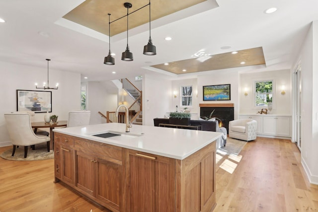 kitchen with pendant lighting, a tray ceiling, a kitchen island with sink, and light wood-type flooring