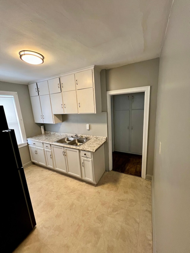 kitchen featuring white cabinetry, black fridge, and sink