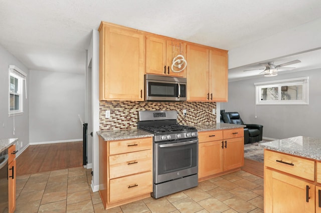 kitchen with a ceiling fan, light brown cabinetry, appliances with stainless steel finishes, decorative backsplash, and baseboards